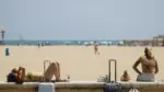 Turistas toman el sol con maletas en la playa de la Malvarrosa, en València